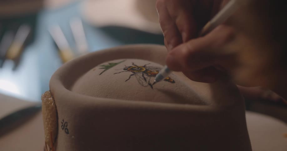 Closeup of a hand painting a bee on a felt hat