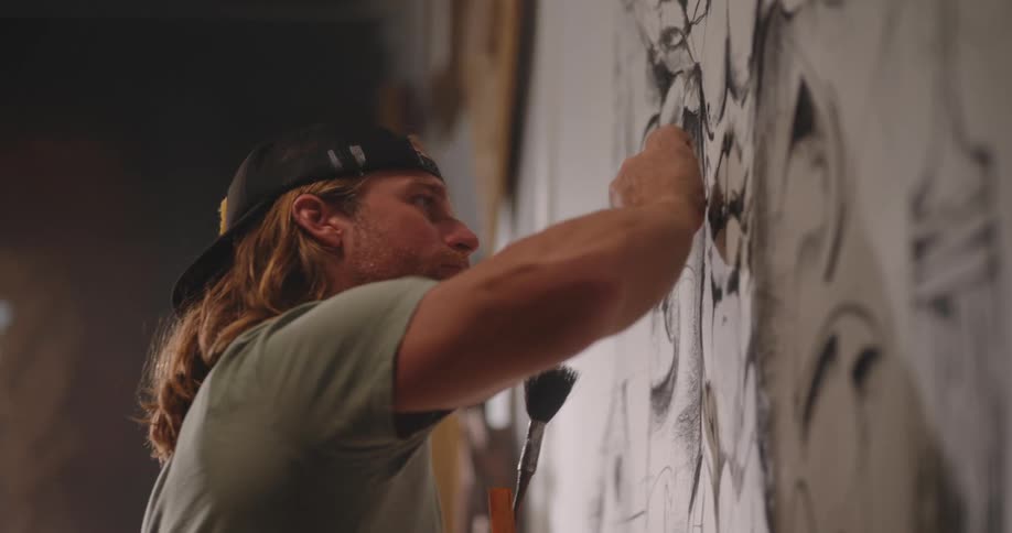 Close up of a young male artist drawing on a white background on the wall in a room during daytime