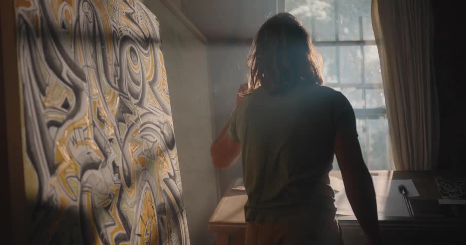 A person drawing at a desk near a sunlit window indoors