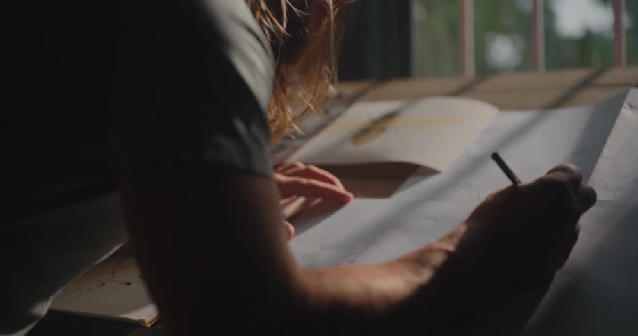 The artist is leaning on the desk and drawing