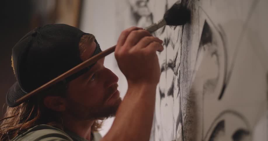 The man is brushing the pencil drawing on the canvas