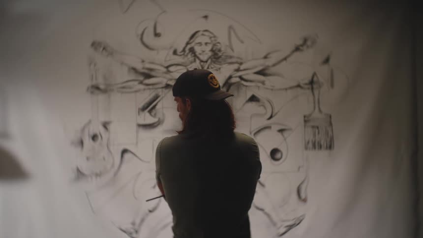 Man wearing a cap observing a large blackandwhite artistic mural