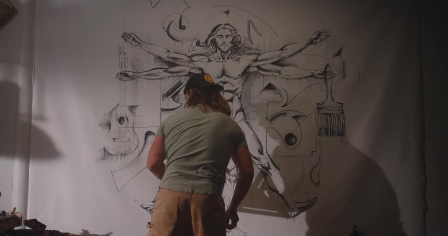 The man is drawing on the large canvas attached to the wall