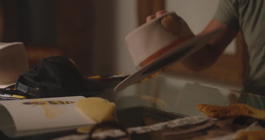 Close up of a young man trying on various hats and a cap placed on a table in a room