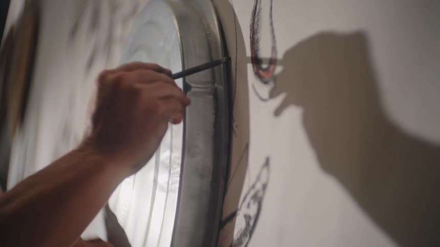 A person sketches with a pencil using a metal stencil on a wall