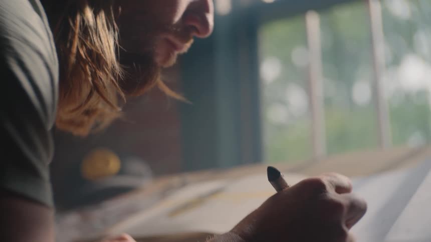 Male hand draws on a sheet illuminated by natural light near the window