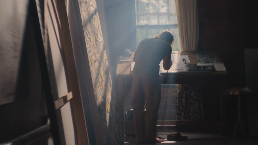 The man is standing at his desk in the studio drawing