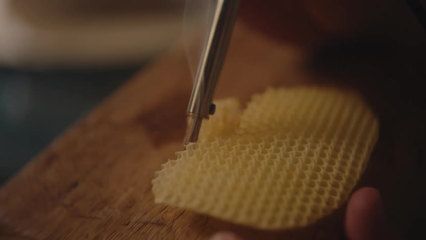 Honeycomb being worked on with a metal tool over a wooden table