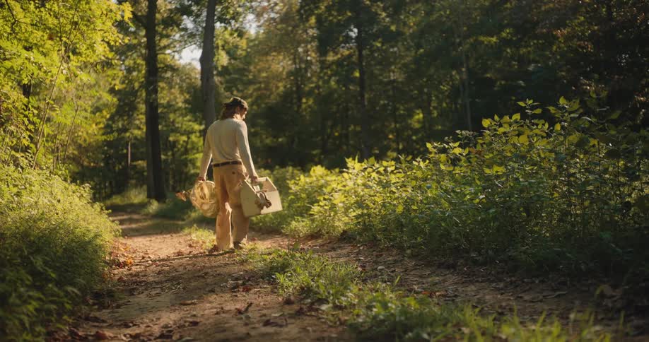 The man walks down the trail with a bee smoker and toolbox