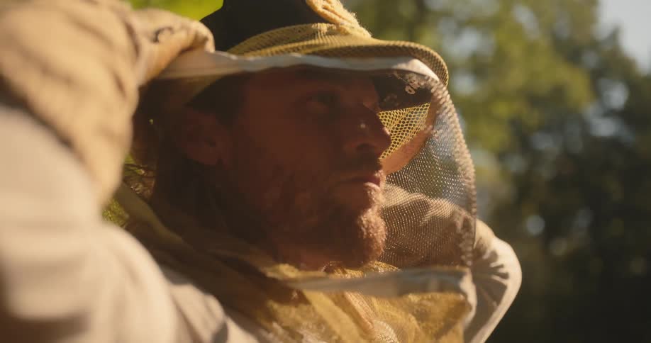 Close up portrait of a young male beekeeper wearing and adjusting a brown suit outdoors during daytime