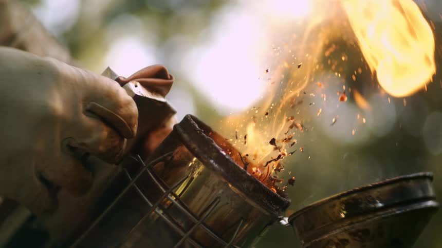 Smoke and flames rise from a metal smoker held by gloved hands