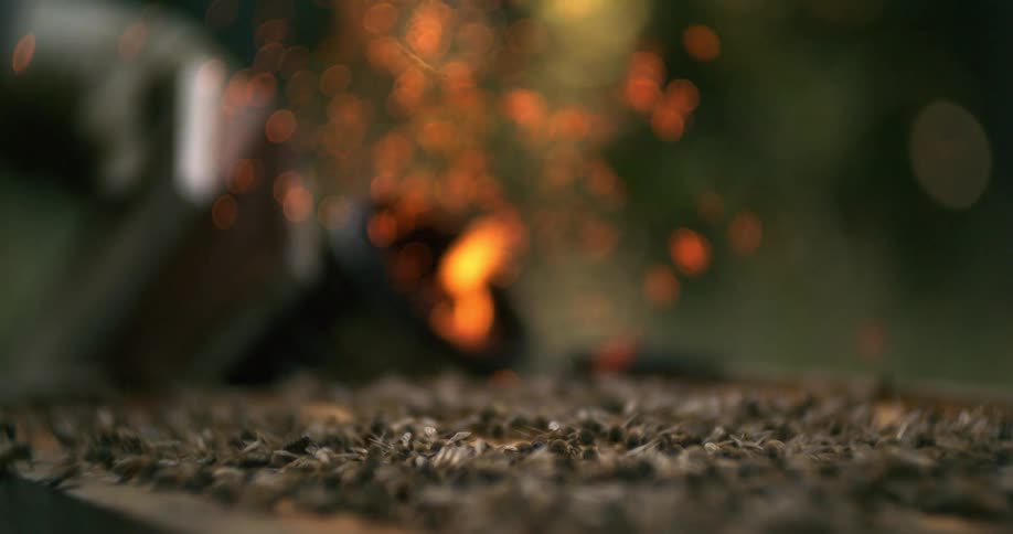 Swarm of bees covers a hive while smoke and sparks rise from a smoker in the background