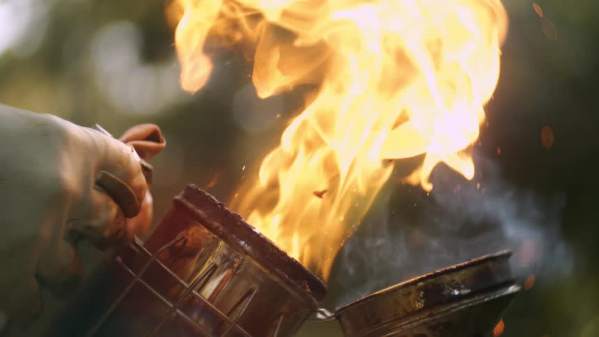 Intense flames and smoke rise from a metal smoker amid greenery