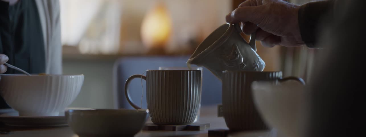 Pouring creamer from green pitcher into coffee in a green mug