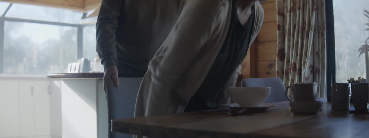 A mature couple preparing a table to take breakfast and the man assists the woman with the chair