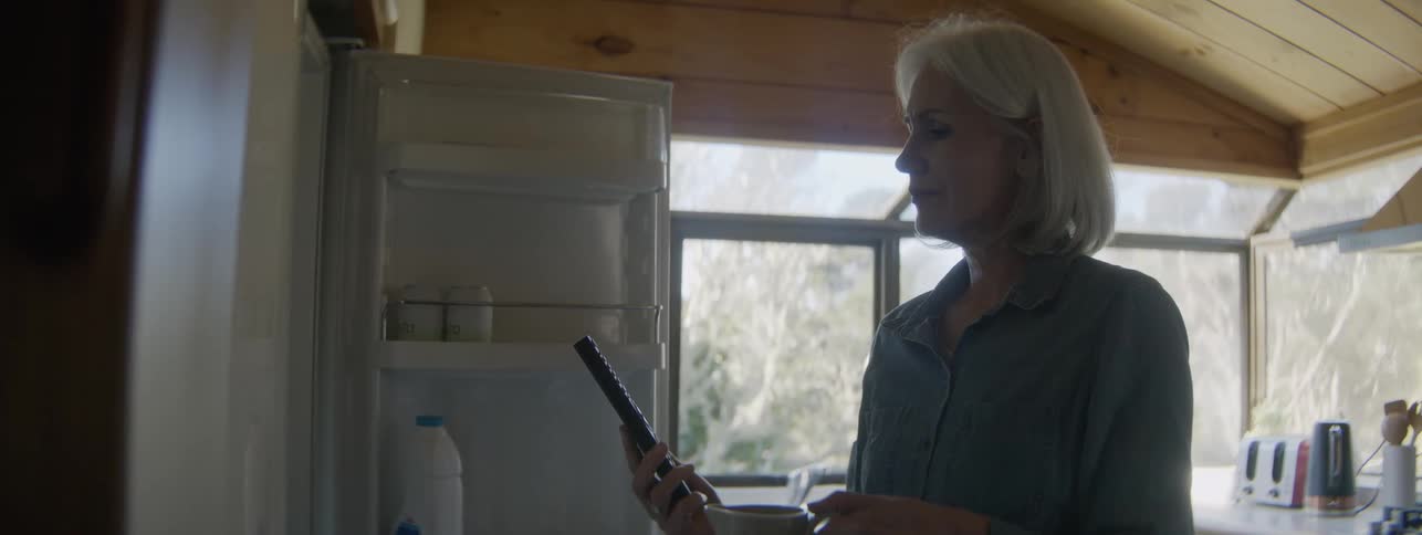 A middle aged woman opens a refrigerator in the kitchen during daytime to find a remote control device from it i