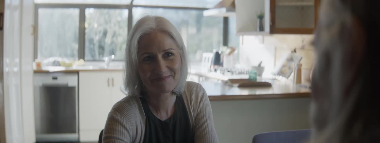 Smiling grayhaired woman sitting in a bright kitchen