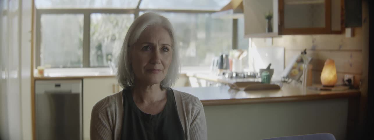 Close up portrait of a middle aged woman sitting at a table in the kitchen during daytime