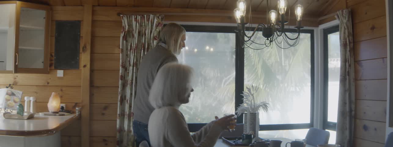 Older couple sits down to eat at the table near their kitchen