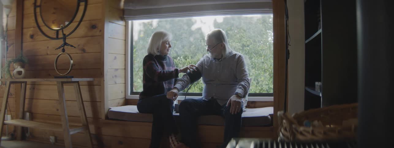 Woman measuring a mans blood pressure while seated by the window