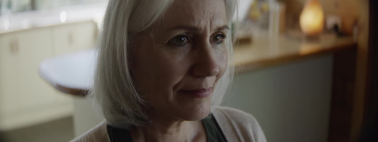 The face of an older woman with short gray hair in an indoor setting sitting on a chair