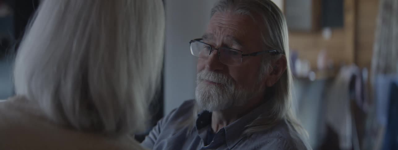 Grayhaired man smiles tenderly while talking to a woman