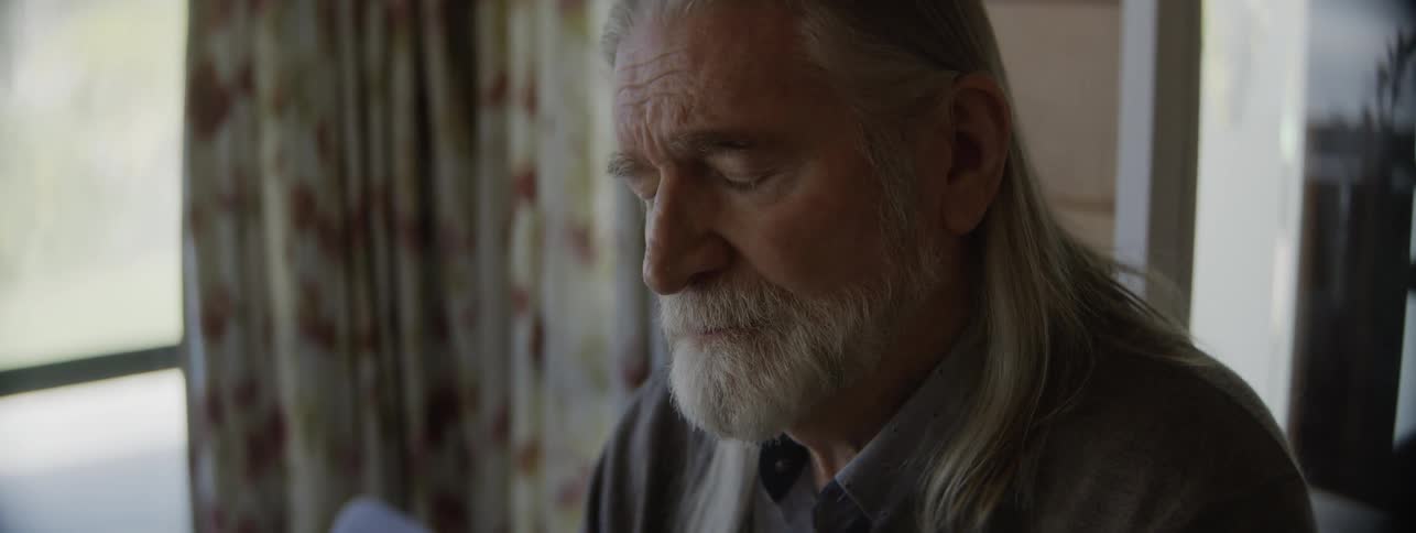 Elderly man with a serious expression sitting near a bright window