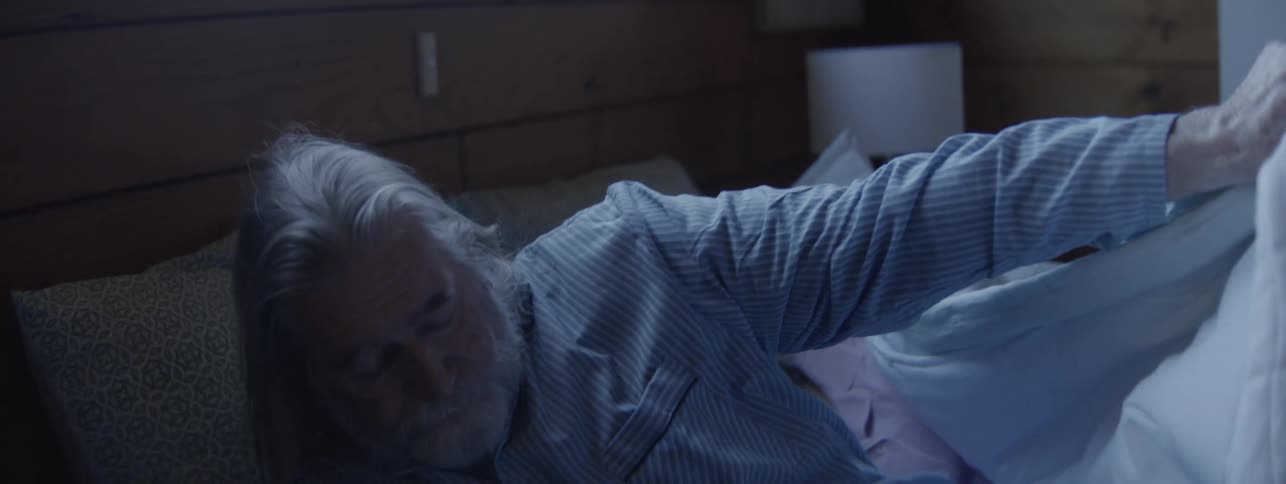 Elderly man in pajamas getting out of bed in a softly lit room with a calm atmosphere