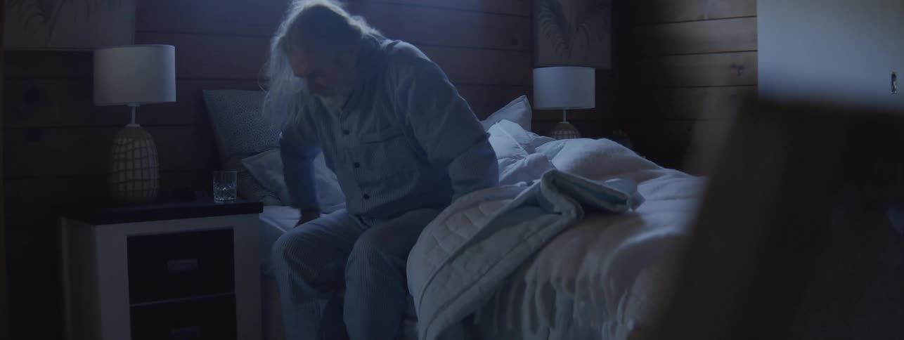 Elderly man lying in bed in a softly lit room with a calm atmosphere