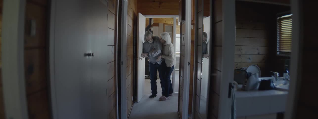 A woman rushes into the hallway to help a man holding his heart and leaning against the wall