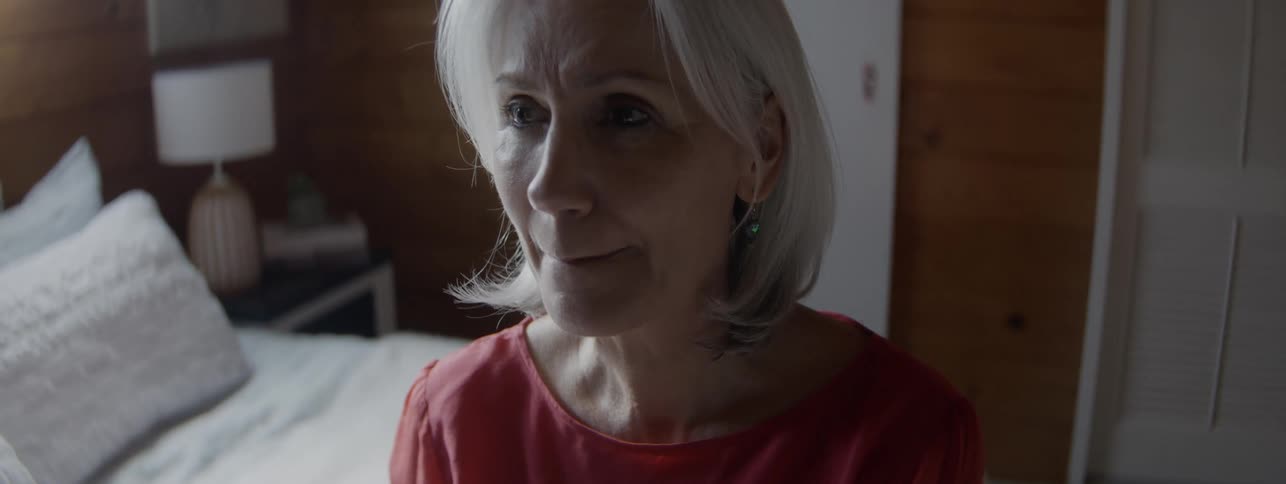 Grayhaired woman looks thoughtful in a softly lit bedroom