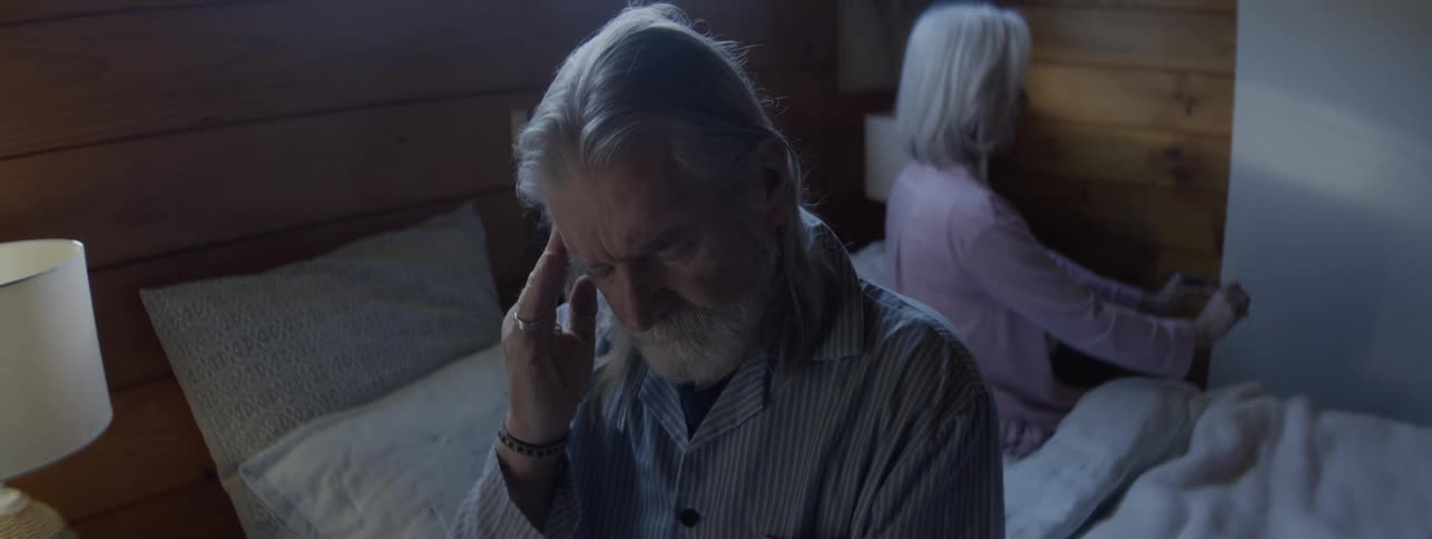 Man sitting on the bed holds his head thoughtfully while woman sits with her back turned