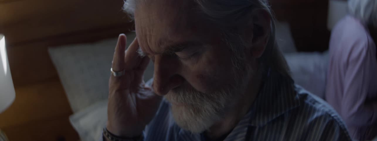 Man touches his head thoughtfully in a softly lit bedroom