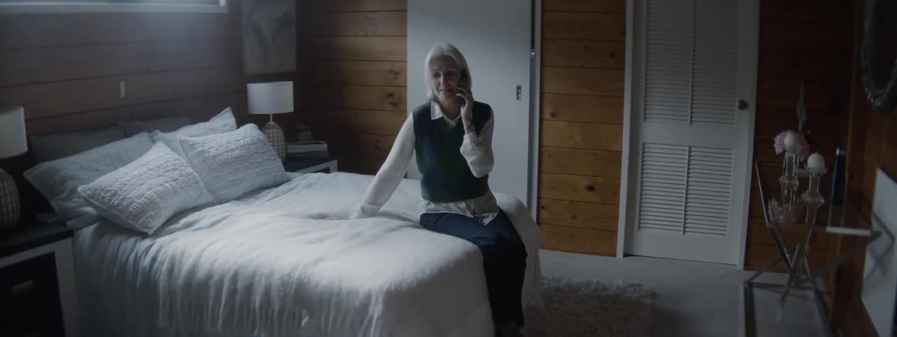 A woman sits on a bed talking on a phone