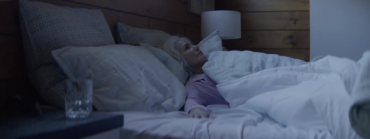 A sleeping middle aged woman wakes up and stands from her bed at sunrise