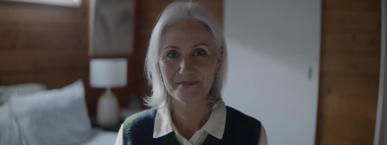 Grayhaired woman smiles gently in a softly lit indoor setting