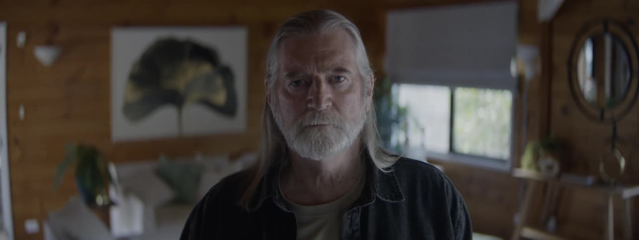 Man with gray hair and beard looks ahead in a cozy setting