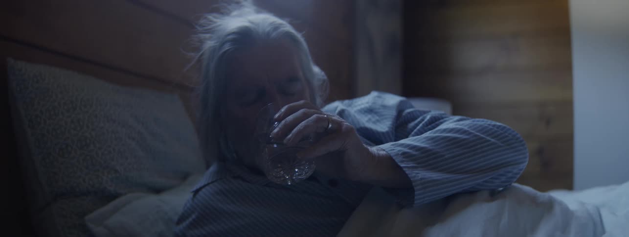 Elderly man wakes up during the night and drinks a glass of water in bed