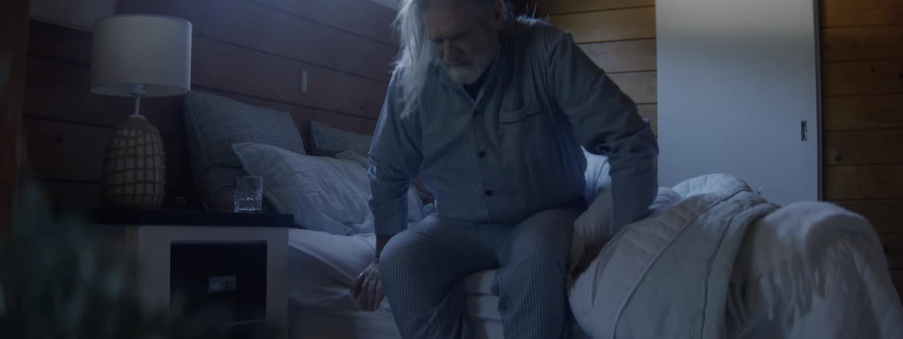 Man in pajamas wakes up and begins to get out of bed in a bedroom lit by natural light