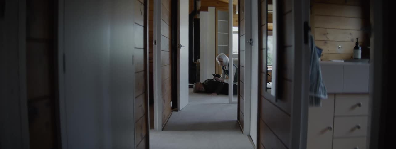 Man collapsed on the floor feeling unwell being assisted by a woman in a hallway