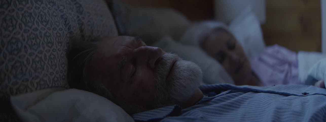 An elderly couple are sleeping in pajamas in a bed