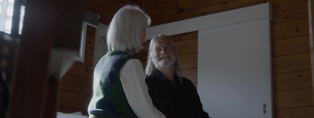 Elderly woman caressing the face of an elderly man seated in a cozy wooden room
