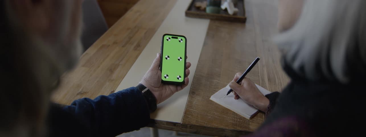 Man holds a smartphone while woman takes notes in a notebook on the table