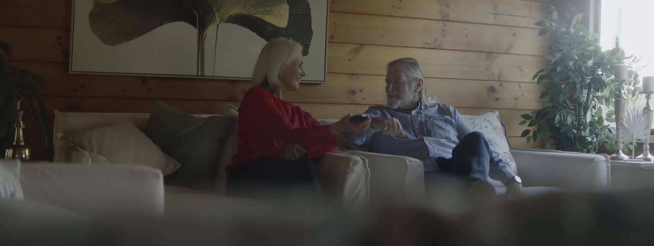 Woman showing something on her phone to a man while they talk sitting on the couch