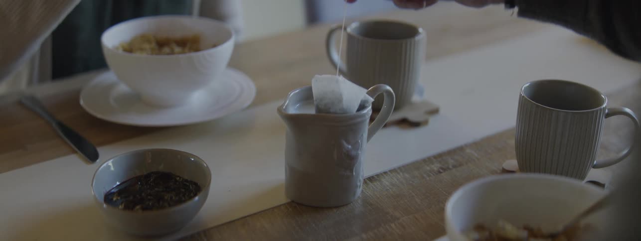 A person developing alzheimer's is confusing the milk jug with the tea cup while trying to dip his tea bag