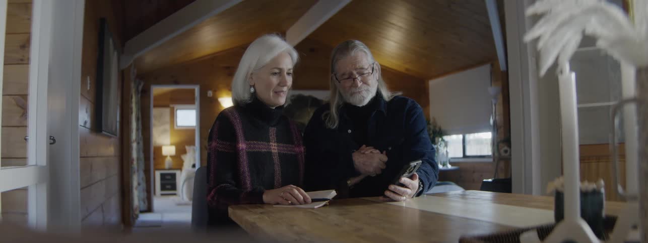 Elderly couple sitting at the table looking at something together on a phone