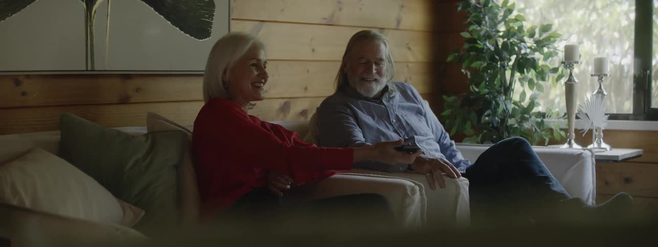 Couple smiles on the couch as the woman shows something on the phone to the man