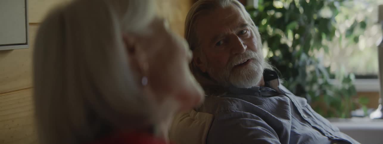Elderly couple smiles while talking in a room lit by natural light