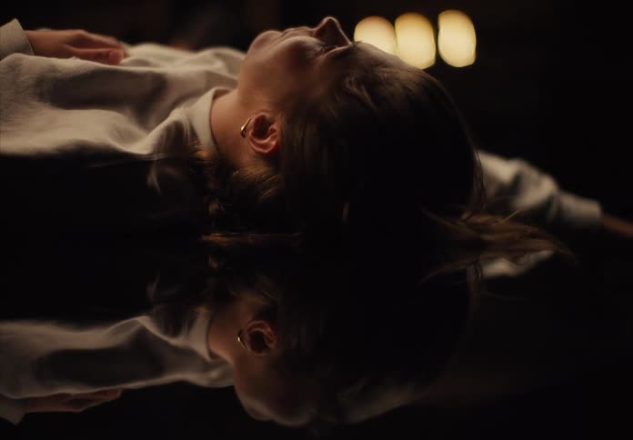 Woman lies on a dark reflective surface while staring upwards