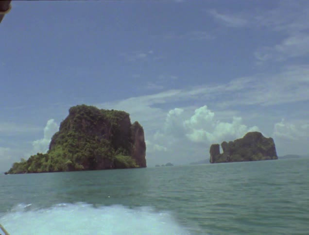 A boat floats on the ocean near rocky islands